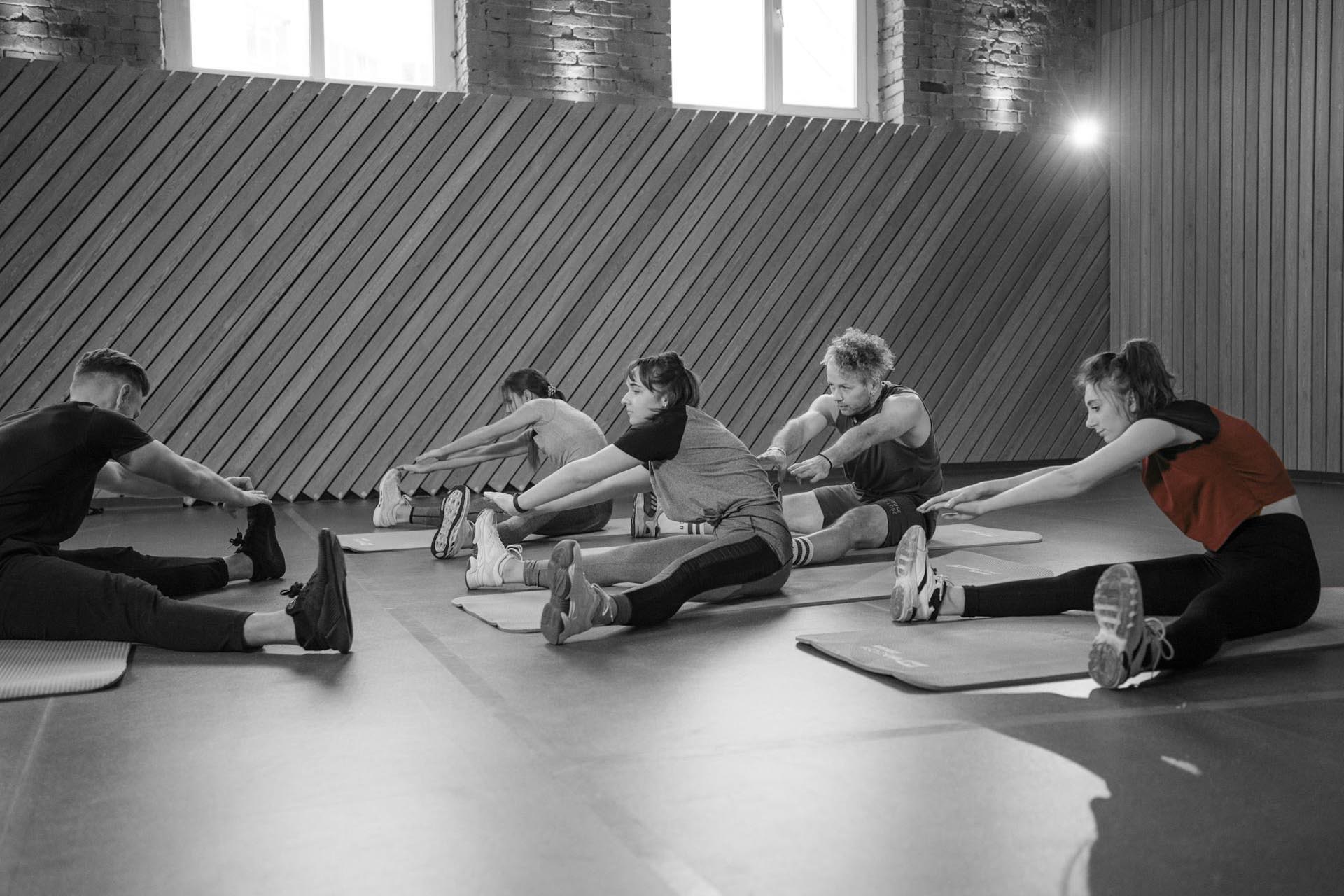 Group fitness class stretching together on mats in a gym, focusing on flexibility and mobility.